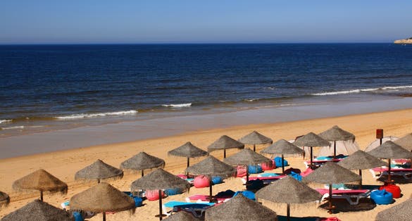 Portugal, Algarve Region, Silves, ArmaÃ?Â§ao de Pera beach with straw sunshades and a crystal clear Atlantic Ocean