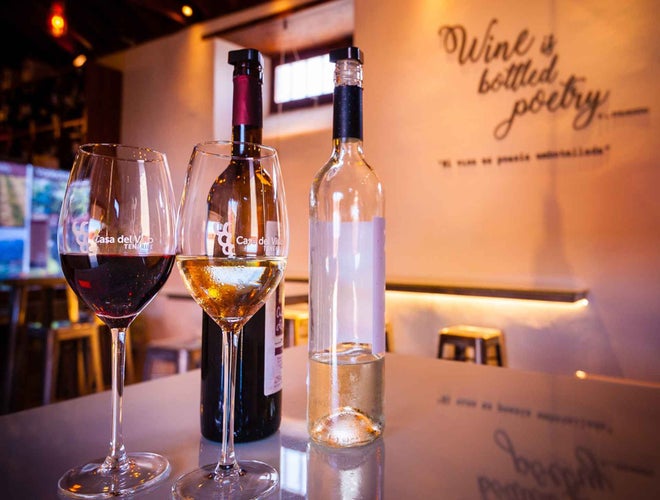 Two wine glasses, one with red wine and the other with white, sit on a table with bottles in a cozy wine bar..jpg