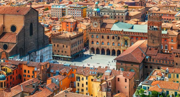 Photo of Italy Piazza Maggiore in Bologna old town tower of town hall with big clock and blue sky on background, antique buildings terracotta galleries.