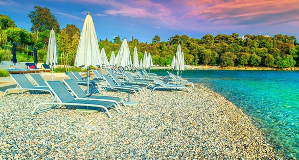 Photo of  gravel beach and seashore. Sun loungers and beach umbrellas at sunset on the beach, Rovinj, Istria region, Croatia.