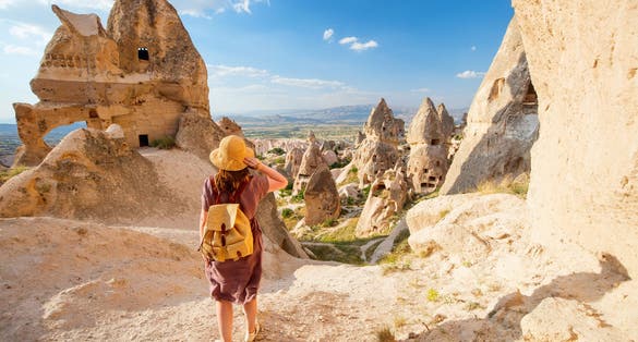 Photo of woman exploring valley with rock formations and fairy chimneys near Uchisar castle in Cappadocia Turkey.