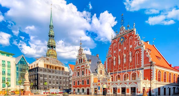 Photo of the Old Town Ratslaukums square, Roland Statue, The Blackheads House and St Peters Cathedral against blue sky in Riga, Latvia. 