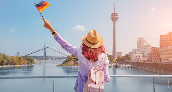 photo of view of A young happy Asian girl with a German flag poses at the Media Harbor and TV-tower in Dusseldorf. Studying language abroad and traveling concept