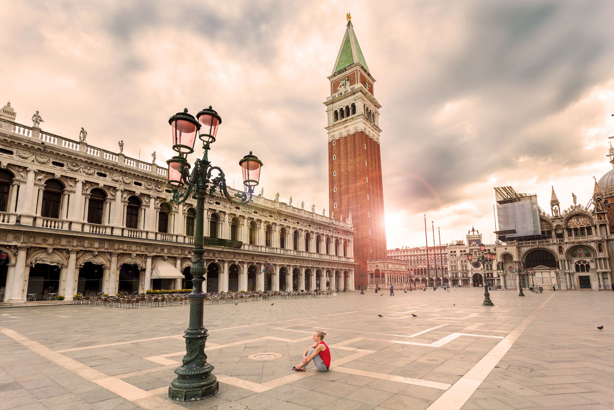 photo of girl female traveler sitting on the piazza san marco in Venice at sunrise and enjoy the area without people. The main square of the old town. Italy.