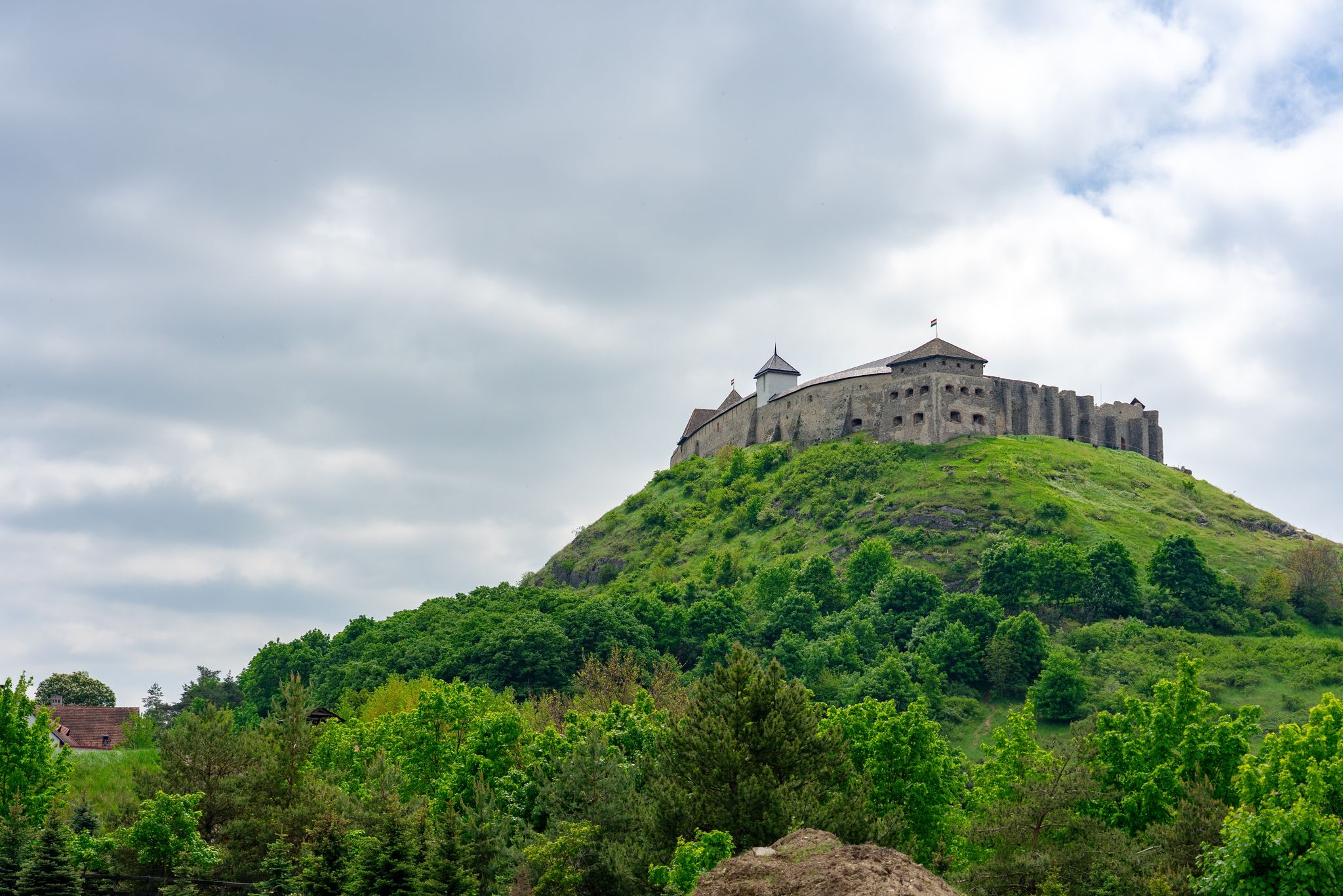 Photo of Sümeg castle on the hill in Hungary spring time with green trees .