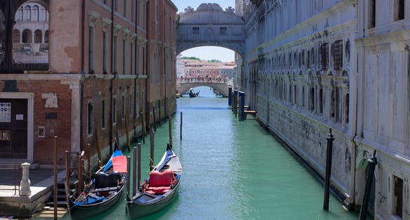 photo of romantic idyllic view of gondolas moored in narrow canal by renaissance facade of Doge's Palace and Ponte de i Sospiri .