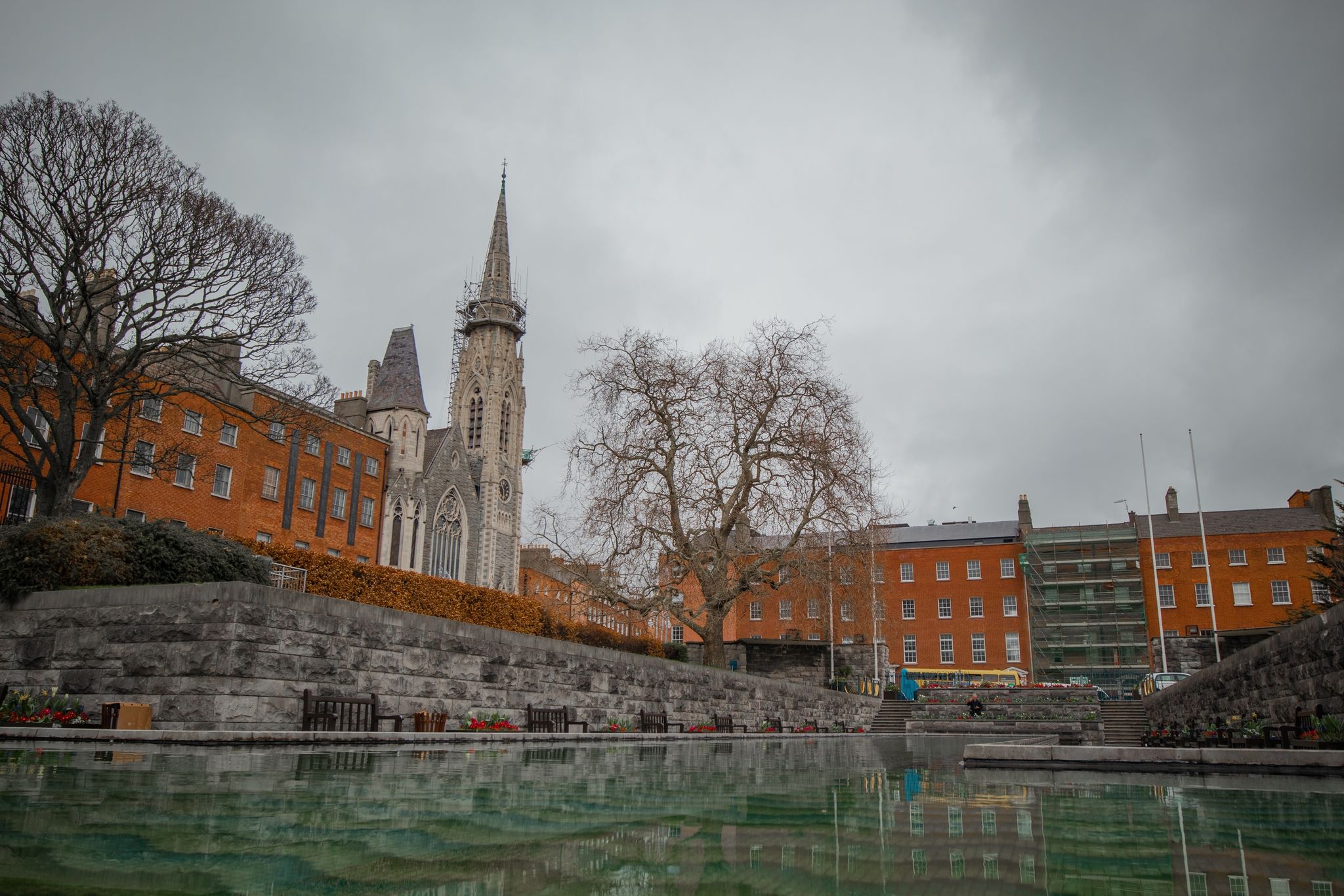 PHOTO OF Garden of remembrance overview in Dublin, Ireland on a gray day. Visible water fountain, flowers and statue. Presbyterian church in the background .