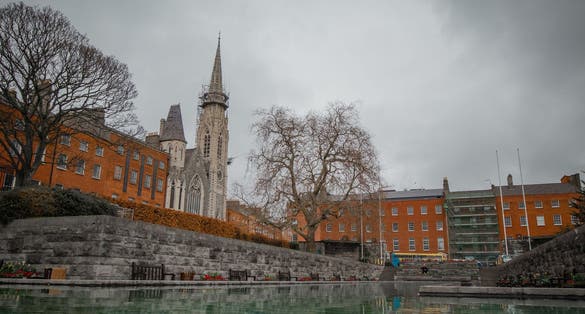 PHOTO OF Garden of remembrance overview in Dublin, Ireland on a gray day. Visible water fountain, flowers and statue. Presbyterian church in the background .