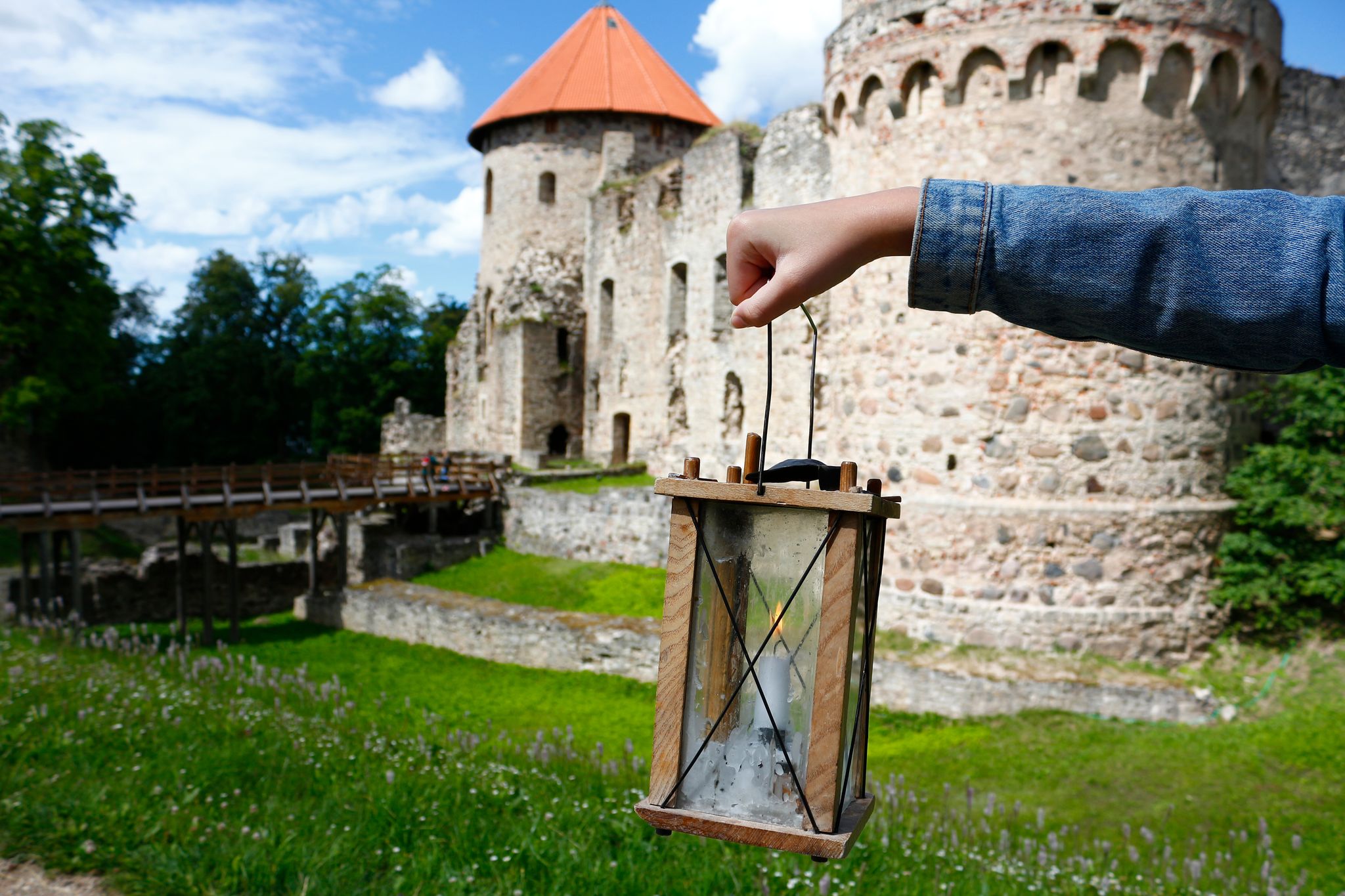 photo of girl's hand holding a candle lantern against the background of the medieval Cēsis castle, Latvia.