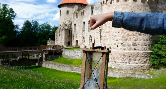 photo of girl's hand holding a candle lantern against the background of the medieval Cēsis castle, Latvia.