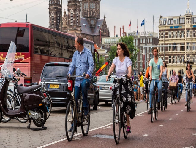 Cyclists riding through central Amsterdam with historic buildings and buses in the background..jpg
