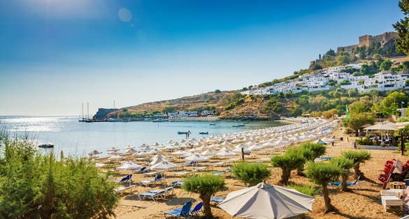 Photo of view of sandy beach in Bay of Lindos, Acropolis in background ,Rhodes, Greece.