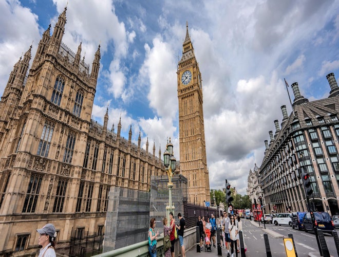 Tourists walk near Big Ben and the Houses of Parliament under partly cloudy skies in London in July..jpg