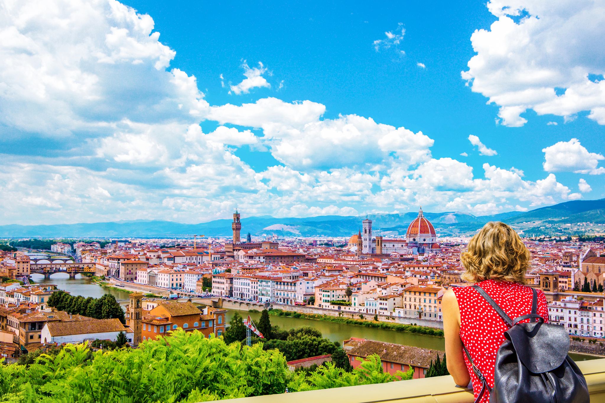 photo of woman tourist in red admires florence firenze (Duomo, arno river, towers, cathedrals, tiled roofs of houses) from piazzale michelangelo, cityscape panorama top view, Florence, Tuscany, Italy.