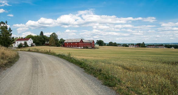 photo of view of rural scene with field and houses under blue sky, Hamar, Hedmark, Norway.