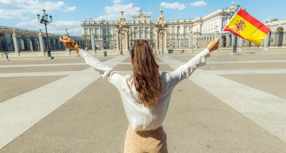 Photo of tourist woman with Spain flag rejoicing against Royal Palace in Madrid.