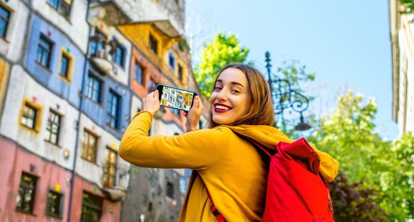 photo of view of Young female tourist photographing with smart phone Hunderwasser building in Vienna, Austria.