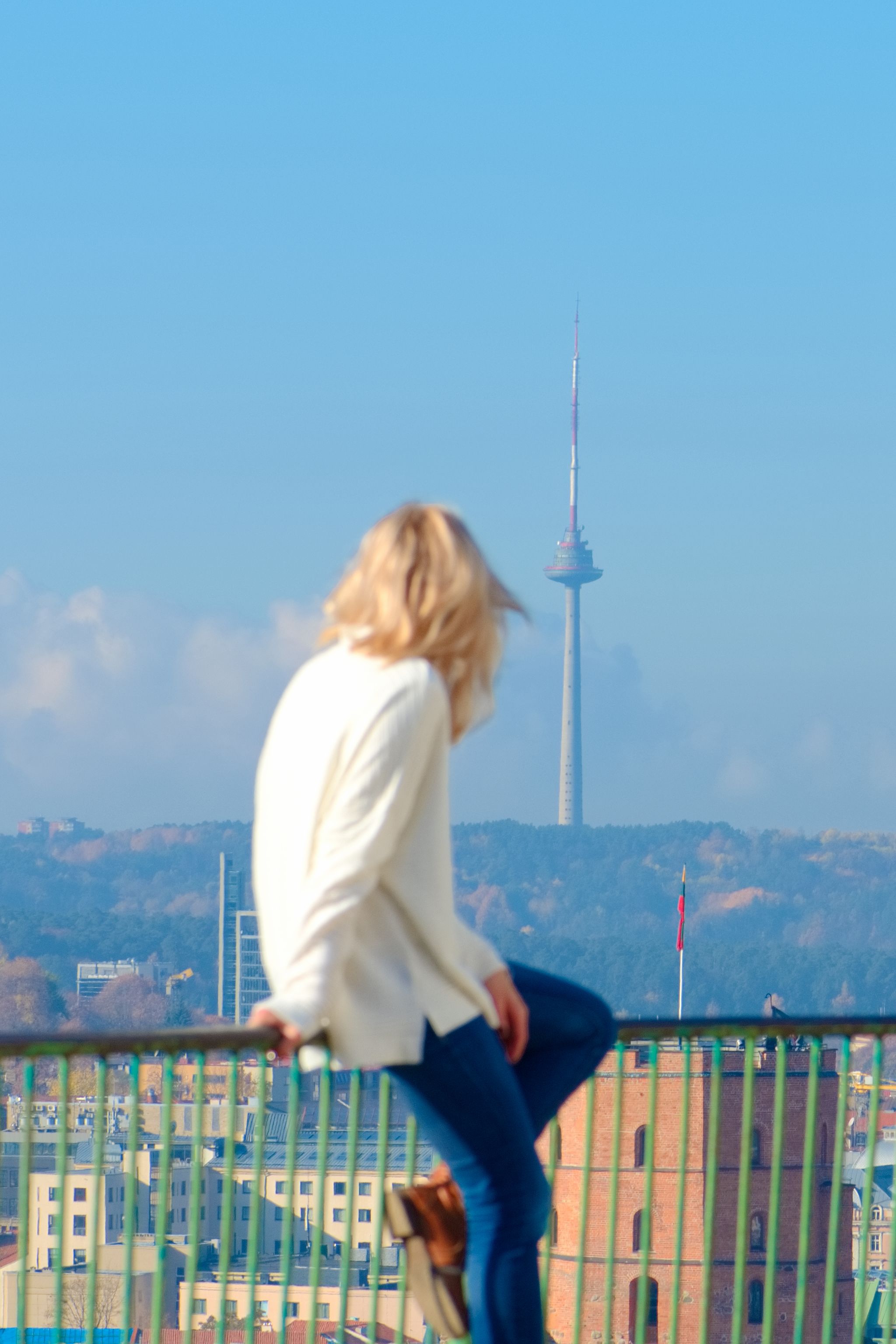 photo of girl out of focus looks at the Vilnius panorama with the TV tower and the gediminas castle in the background.