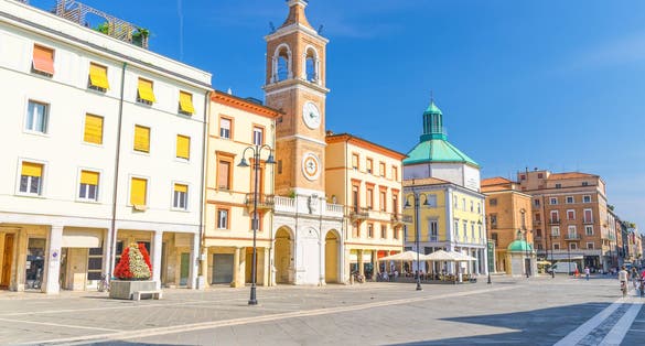 Photo of Piazza Tre Martiri Three Martyrs square with traditional buildings with clock and bell tower in old historical touristic city centre Rimini with blue sky background, Emilia-Romagna, Italy