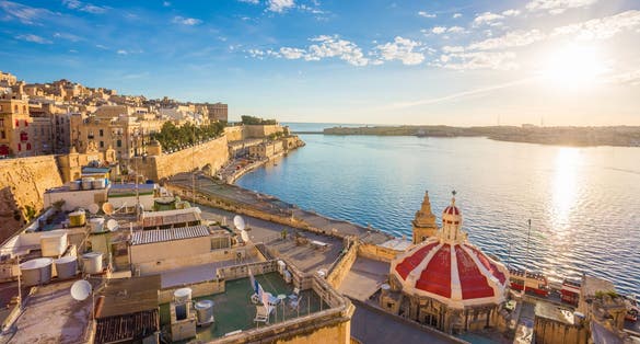 Photo of beautiful sunrise at the Grand Harbour of Malta with the ancient walls of Valletta on a sunny summer morning with blue sky and sunrays.