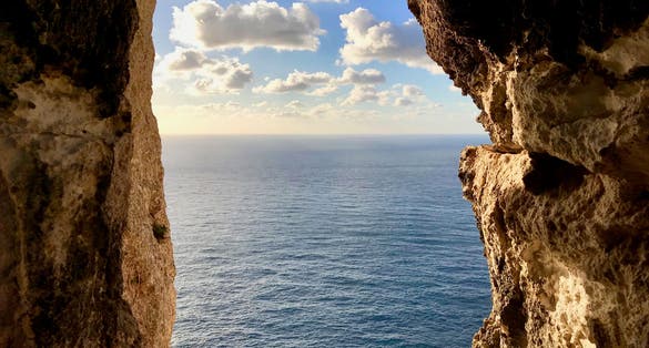 Photo of sunset and sea seen through a rocky window from Dingli Cliffs, Malta.