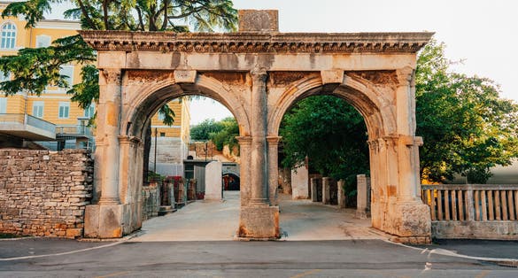 Photo of an aged stone gate surrounded by lush green on a sunny day in Pula, Istria, Croatia.