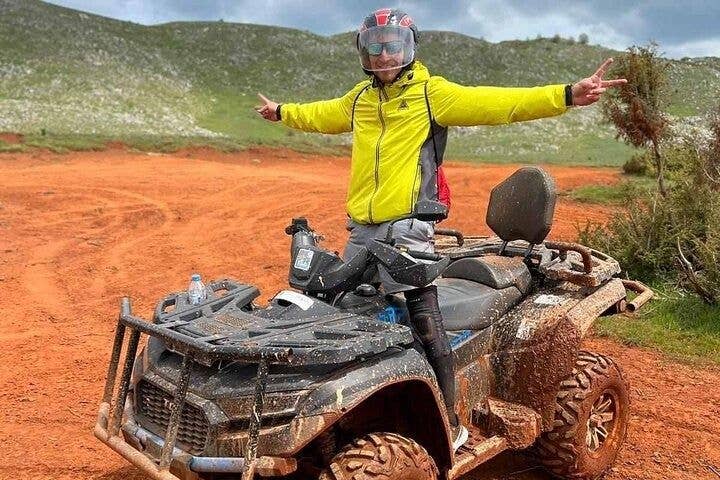 A person in a yellow jacket and helmet stands on a muddy ATV, making a peace sign, in Ohrid, North Macedonia..jpg