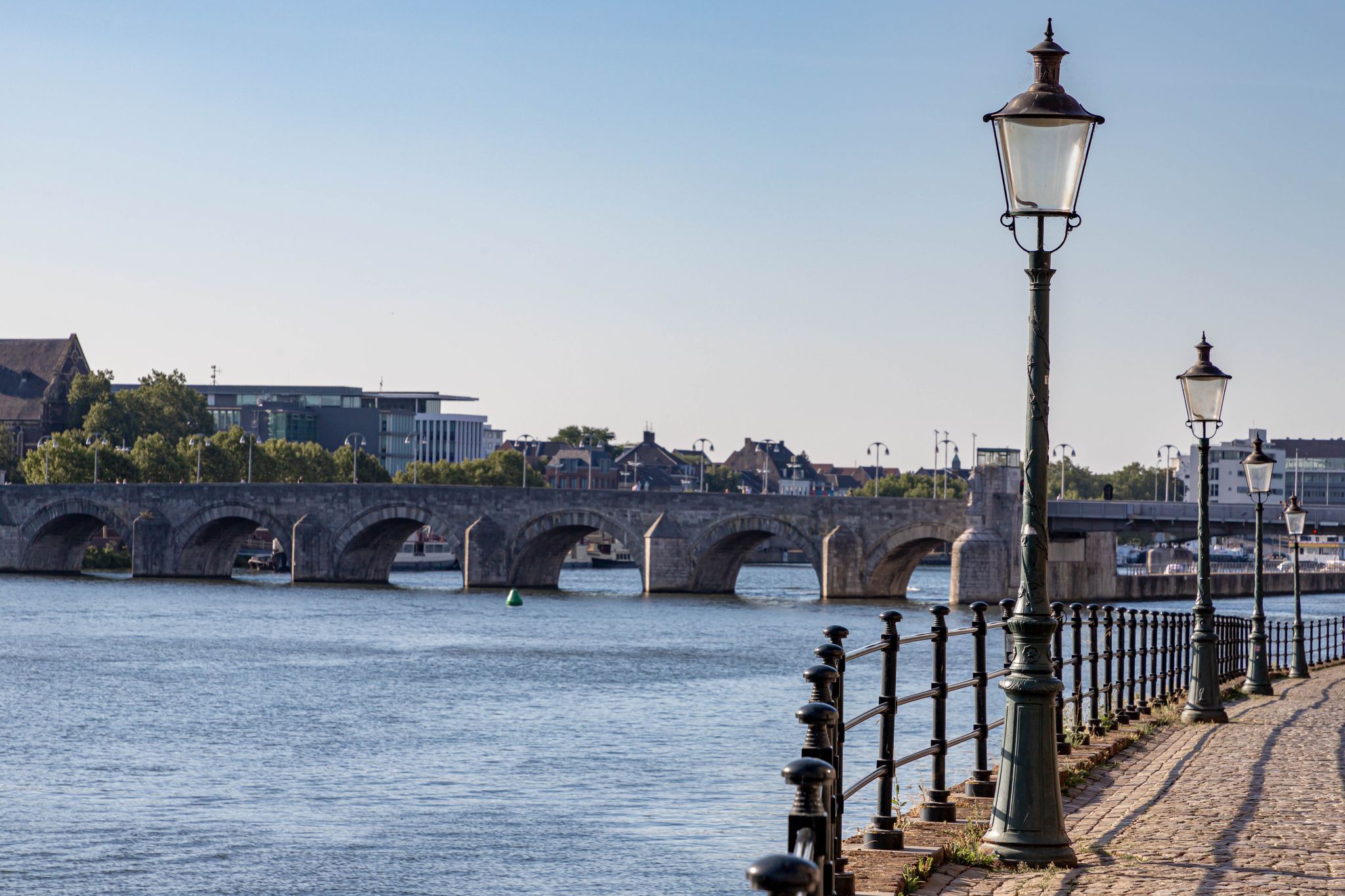 photo of selective focus of light pole along the river Maas with blurred view of the Saint Servatius bridge in Maastricht, Netherlands.