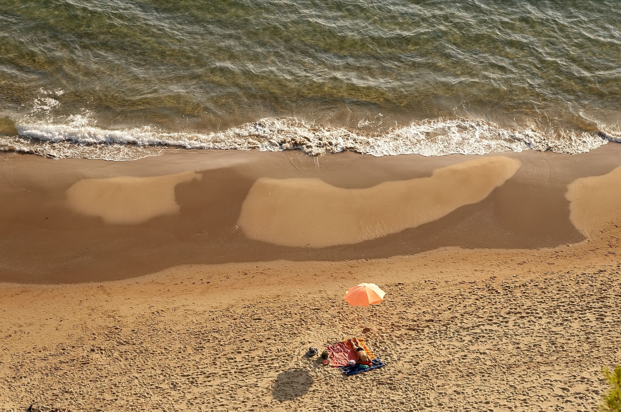 Yellow sand beach with dark parts left by the backwash of the sea and small umbrella, Gaeta, Italy.