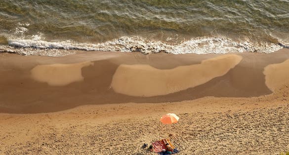 Yellow sand beach with dark parts left by the backwash of the sea and small umbrella, Gaeta, Italy.