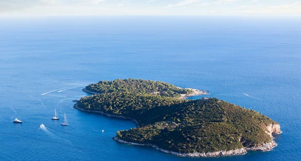Photo of beautiful aerial view of green Island Lokrum Near Dubrovnik Surrounded by a Big Blue Sea, Sailboats, Boats and a Yacht.
