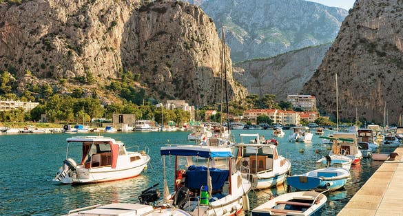 Photo of fishing and sailing boats on the Cetina river in Omis resort. Anchored boats and high mountains in background, Omis, Makarska riviera, Dalmatia, Croatia.