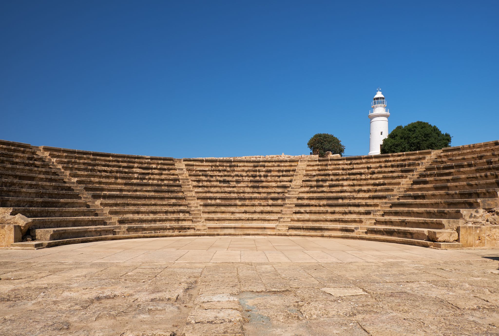 Photo of the view of the central square (agora) of ancient city of Nea Pafos with theater Odeun and lighthouse on the background. Paphos Archaeological Park. Cyprus.