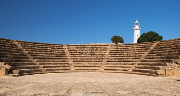 Photo of the view of the central square (agora) of ancient city of Nea Pafos with theater Odeun and lighthouse on the background. Paphos Archaeological Park. Cyprus.