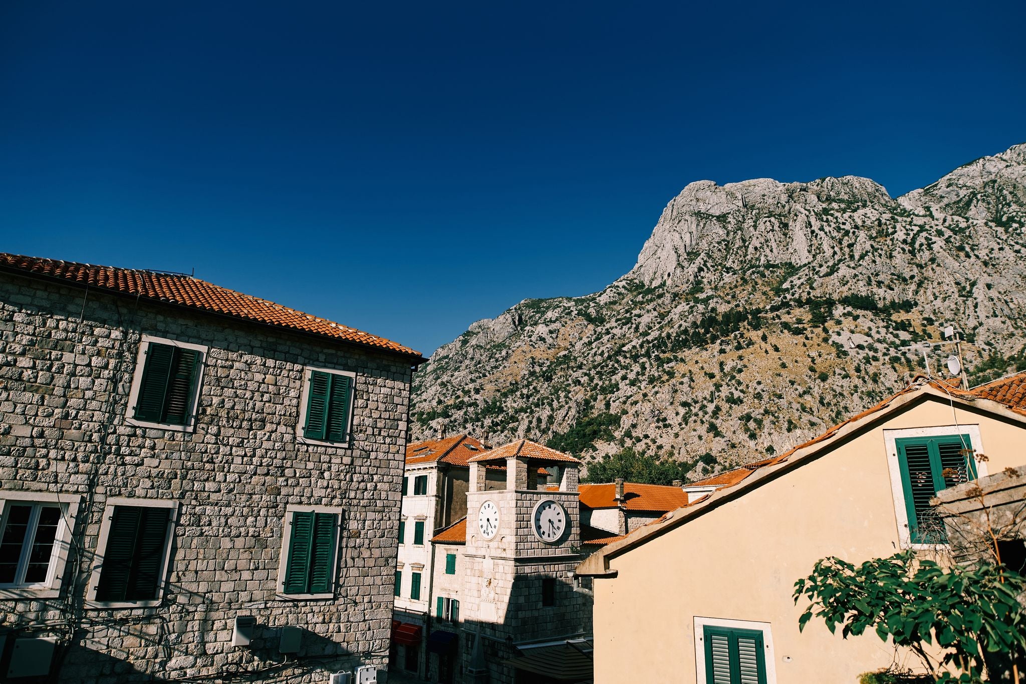 Photo of Clock tower among old stone houses at the foot of the mountains. Kotor, Montenegro.