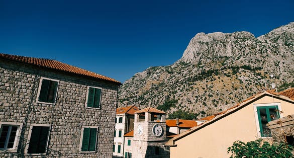 Photo of Clock tower among old stone houses at the foot of the mountains. Kotor, Montenegro.