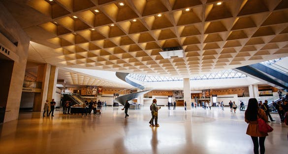 Photo of entrance to the Louvre. Visitors in the lobby under a glass pyramid, Paris, France.