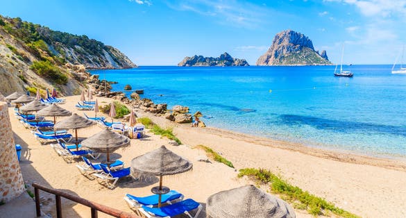 Photo of  Cala d'Hort beach with sunbeds and umbrellas and beautiful azure blue sea water, Ibiza island.