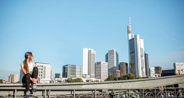 Photo of tourist woman sitting on the bridge with great view on the modern city of Frankfurt.