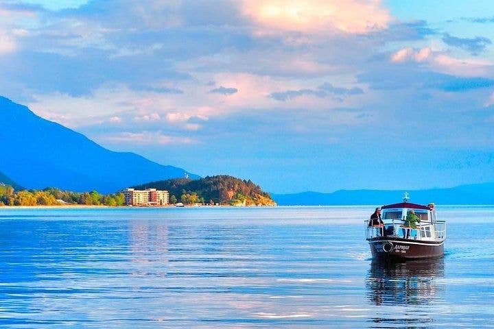 A small boat floats on the calm waters of Lake Ohrid, North Macedonia, with mountains and a hotel in the background..jpg