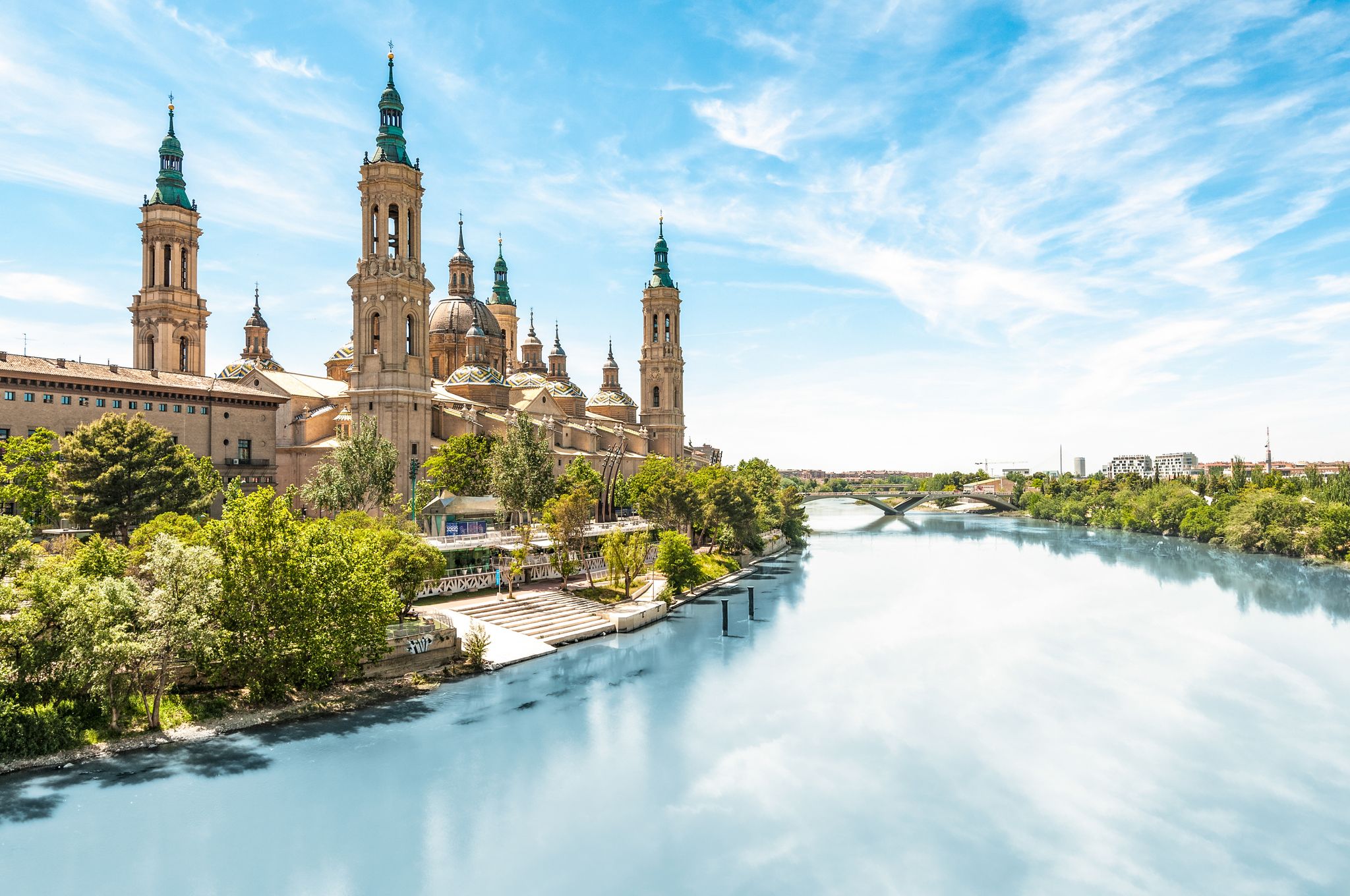 Photo of Scenery landscape with Basilica of Our Lady of Pillar. Blue sky reflects in clear water. Green trees along river.