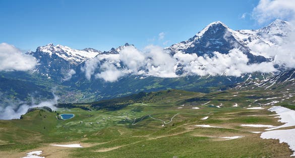 photo of clouds covering snowy mountains and Swiss Alps landscape with meadow and green nature at Männlichen, Grindelwald mountains, Bernese Alps, Switzerland.