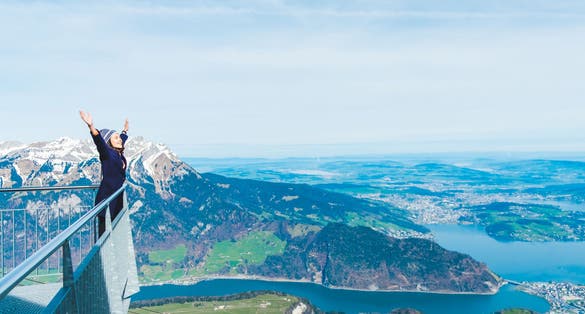 photo of young woman tourist standing with hands up achieving with the snow mountain background, Mt. Stanserhorn in Switzerland.