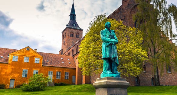 Photo of Monument from 1888 for the Danish author Hans Christian Andersen, Odense cathedral in background, Denmark.