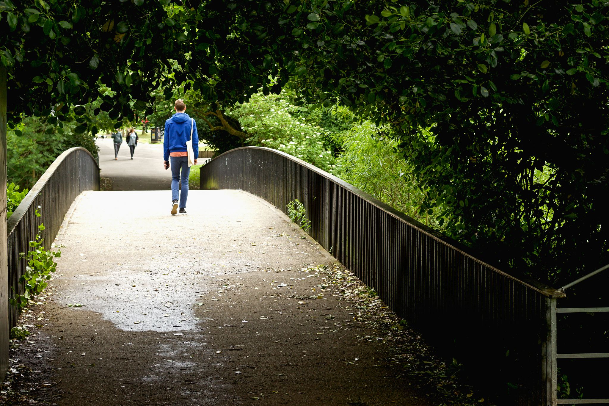 Young man crossing a bridge in to Kelvingrove Park, Glasgow. A peaceful wander in the park.