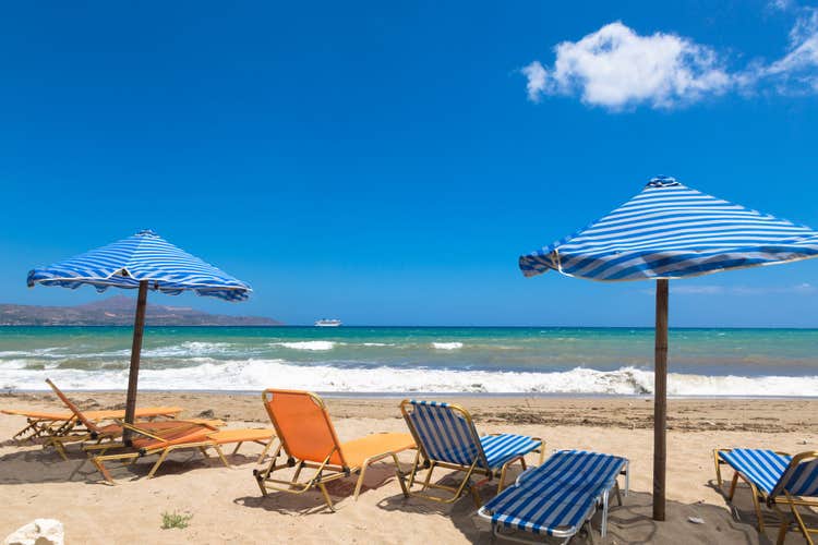Kalyves beach in the Crete in Greece. Blue umbrella and yellow beach beds on the background of sea.