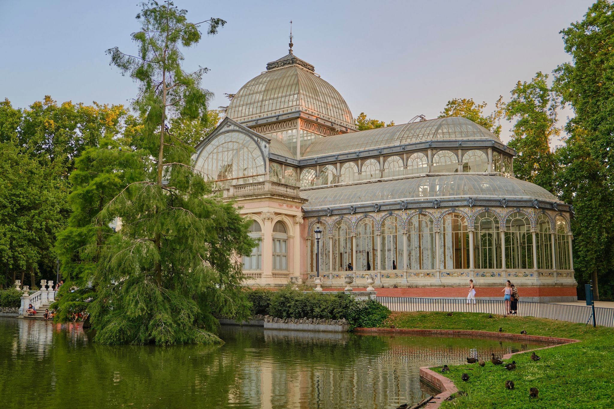 Photo of view of the Palacio de Cristal, one of the most popular tourist attractions in El Retiro Park, Madrid city, with a lake and ducks in front.