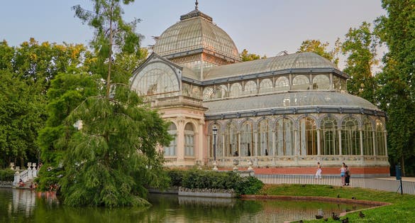 Photo of view of the Palacio de Cristal, one of the most popular tourist attractions in El Retiro Park, Madrid city, with a lake and ducks in front.