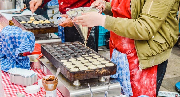 Photo of Two vendors prepare Traditional Dutch poffertjes at the Albert Cuyp market in Amsterdam.