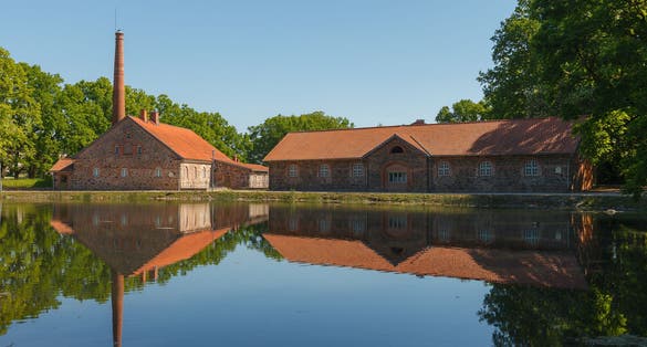 Photo of Olustvere manor in the summer time. The manor's vodka factory buildings are reflected in the park's pond, Estonia.